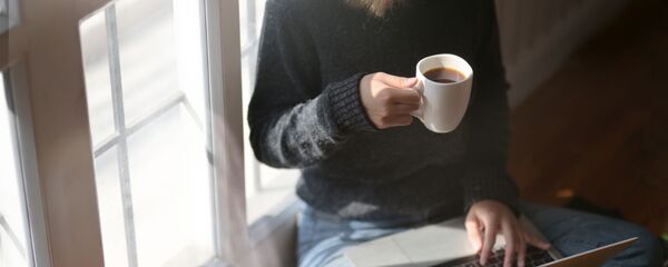 Женщина пьет кофе во время работы за ноутбуком Женщина пьет кофе во время работы за ноутбуком - Sputnik Latvija