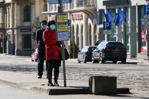 Женщина и мужчина в защитных масках на остановке общественного транспорта в Риге - Sputnik Латвия