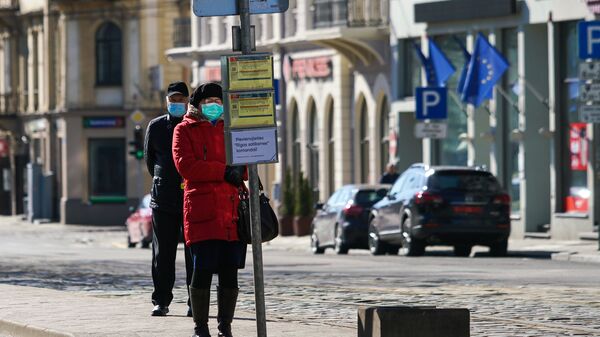 Женщина и мужчина в защитных масках на остановке общественного транспорта в Риге - Sputnik Latvija