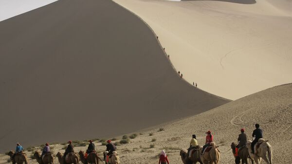 Туристы катаются на верблюдах на краю пустыни, которая угрожает поглотить древний китайский город Дуньхуан  - Sputnik Латвия