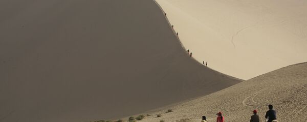 Туристы катаются на верблюдах на краю пустыни, которая угрожает поглотить древний китайский город Дуньхуан Туристы катаются на верблюдах на краю пустыни, которая угрожает поглотить древний китайский город Дуньхуан - Sputnik Латвия