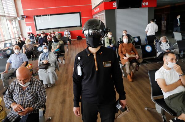 Сотрудник службы безопасности в тепловизионном шлеме следит за пассажирами, ожидающими посадки на рейс в аэропорту Стамбула - Sputnik Латвия
