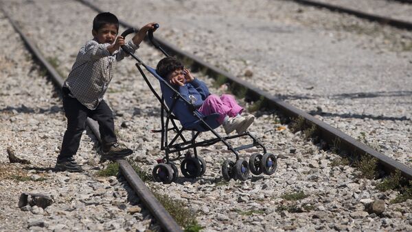 Мальчик везет коляску с ребенком в лагере беженцев в Идомени, Греция - Sputnik Латвия