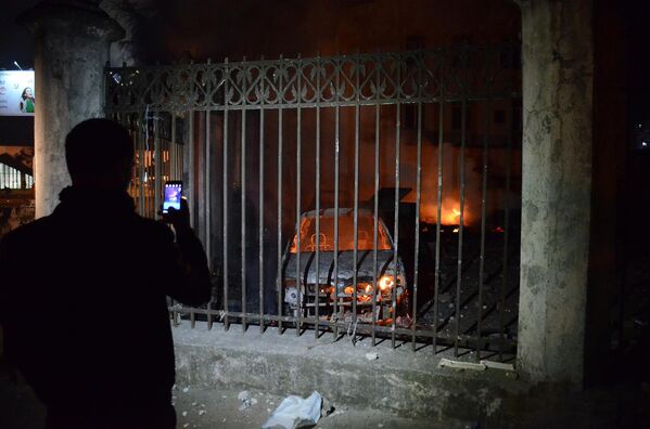 Человек фотографирует на смартфон сожженные в ходе беспорядков в Батуми машины - Sputnik Латвия