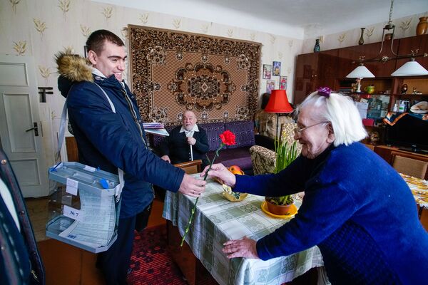 Член мобильной избирательной бригады дарит цветок участнице голосования - Sputnik Латвия